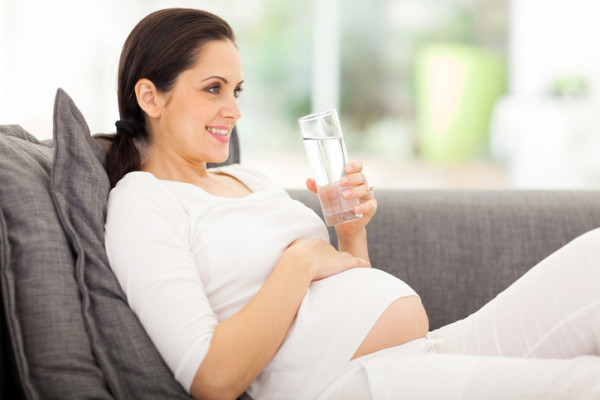 pregnant woman drinking water while lying on a sofa
