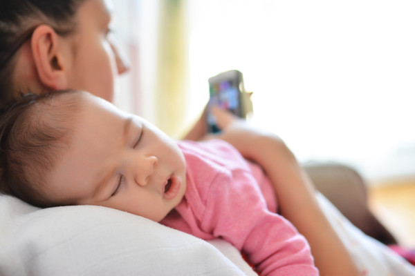 Mother In Bed With Baby Daughter Checking Mobile Phone