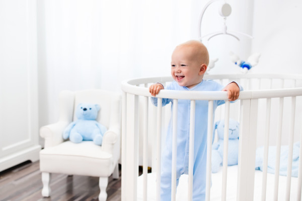 Baby boy standing in bed in white nursery