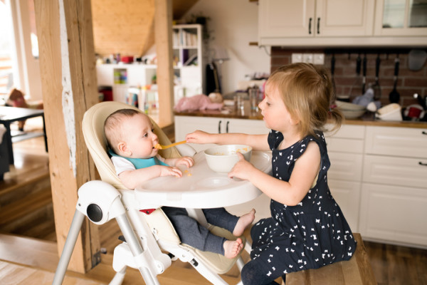 Cute little girl at home feeding her baby brother.