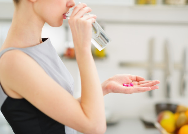 Closeup on young housewife eating pills and drinking water