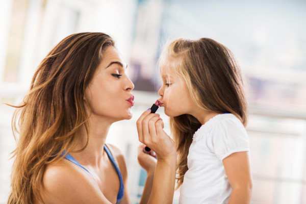 Young mother applying lipstick on her daughter.